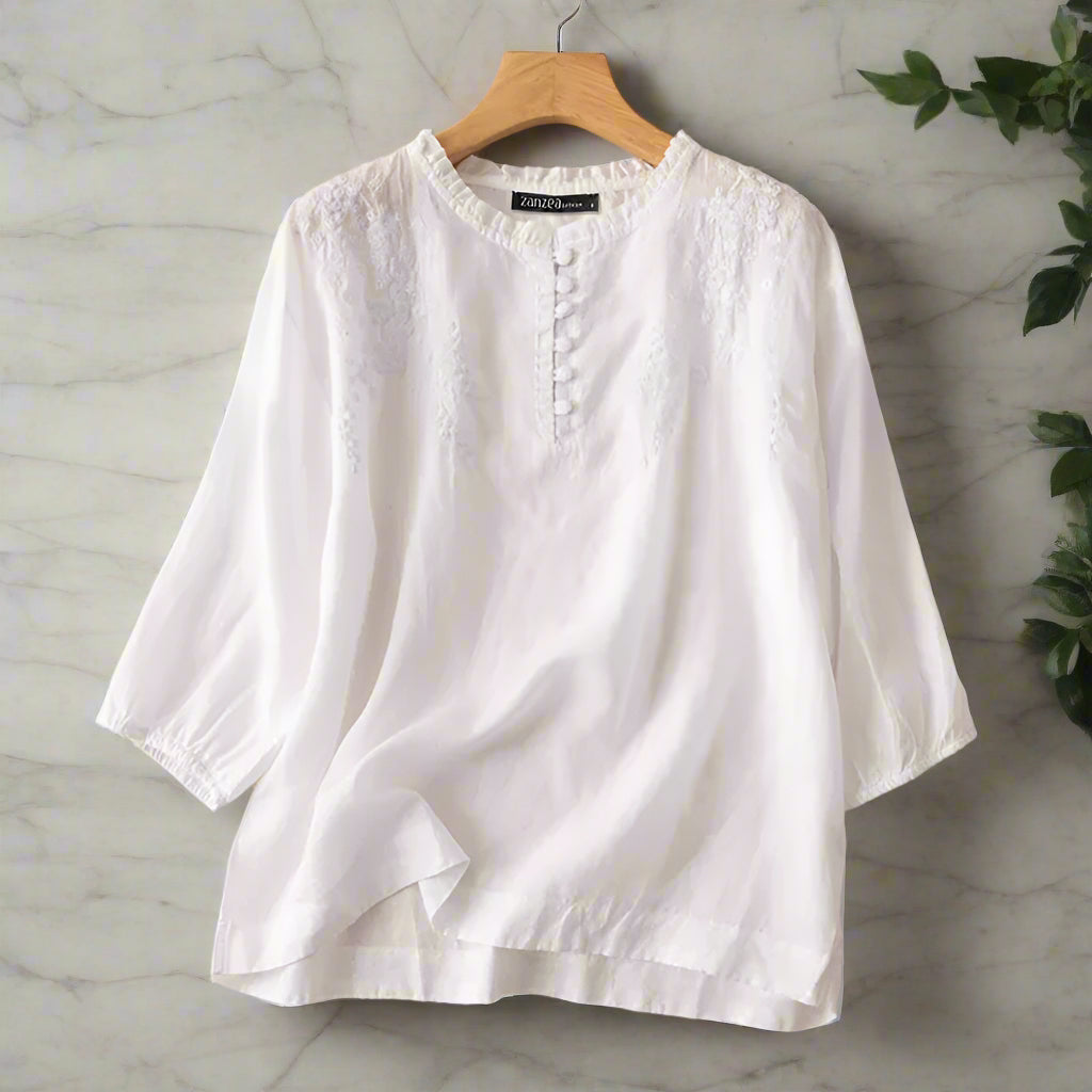White blouse on a hanger with ZANZEA branding against a beige background