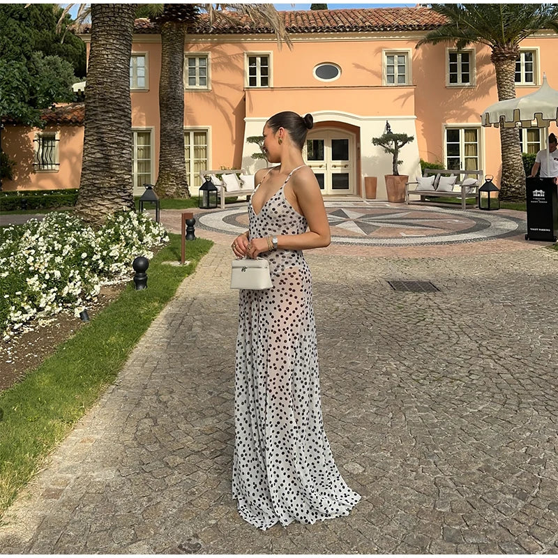 Woman in a polka dot dress standing in front of a building with palm trees and flowers.