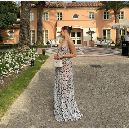 Woman in a polka dot dress standing in front of a building with palm trees and flowers.