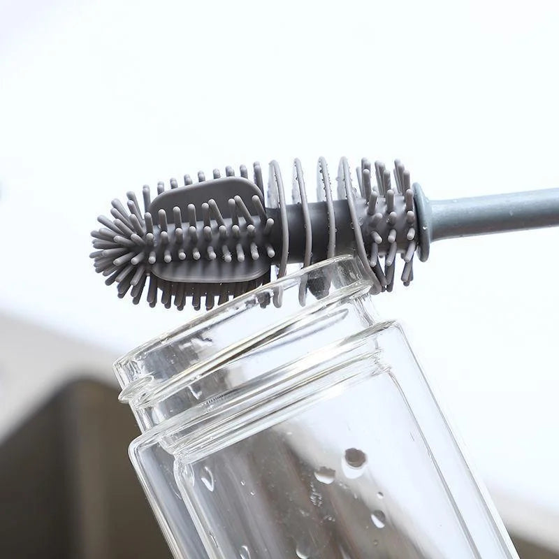 Bottle cleaning brush with bristle head and rubber handle being used on a clear bottle.