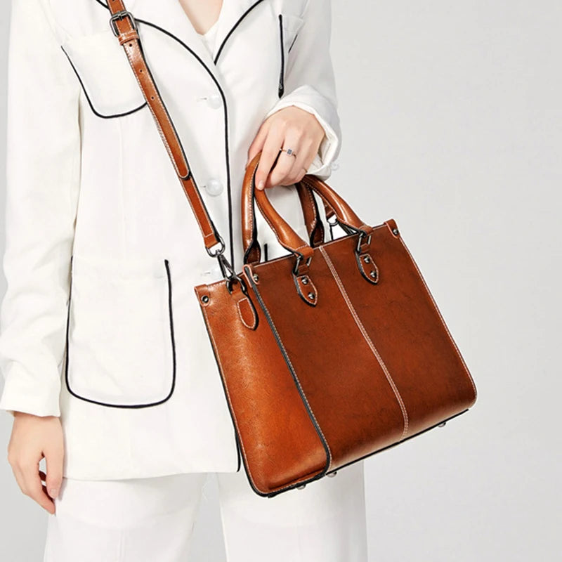 Brown handbag held by a person wearing a white outfit on a light gray background