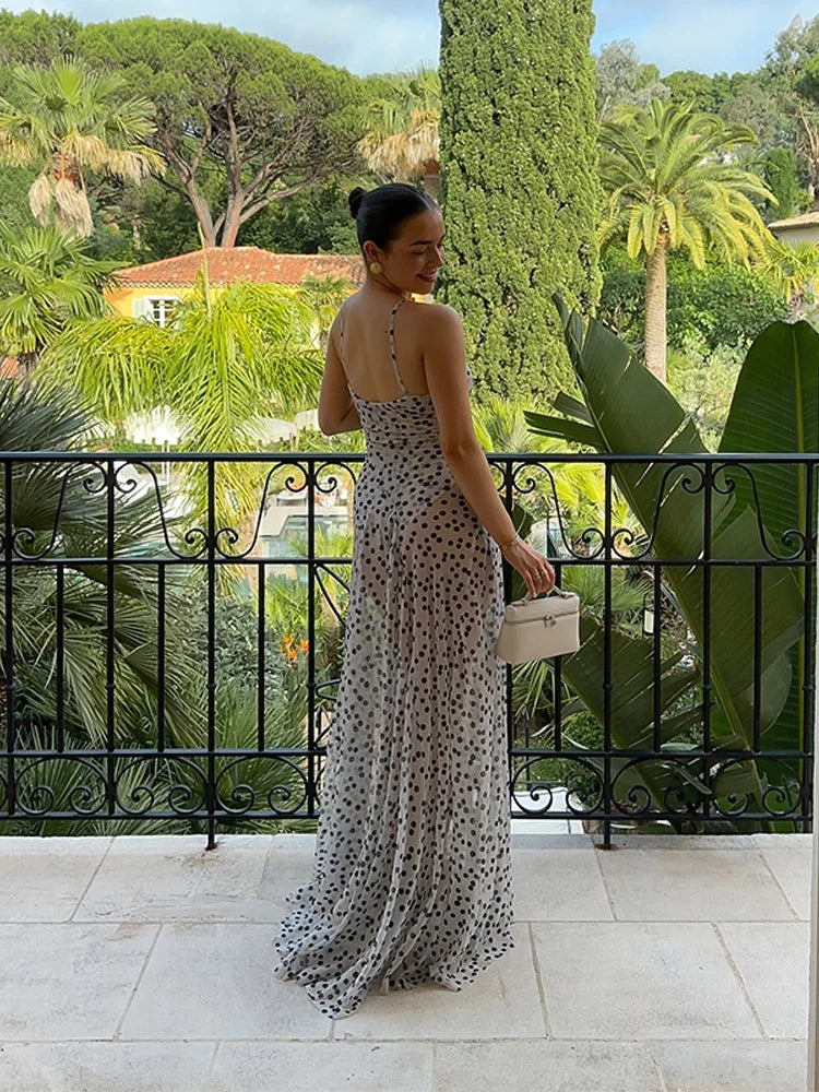 Woman in a polka dot dress standing on a balcony with a scenic view of trees and buildings.