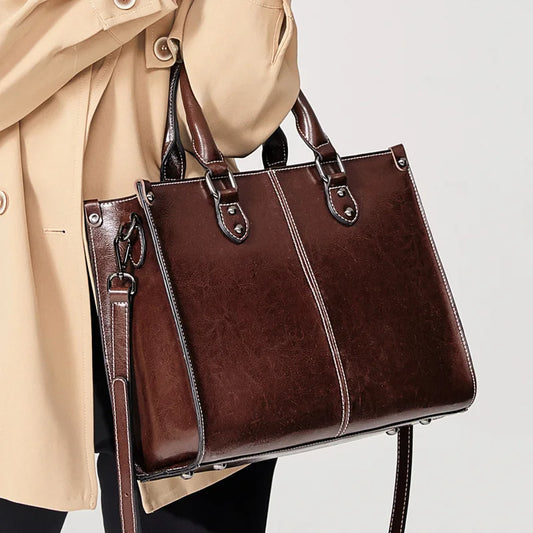Brown leather handbag held by a person wearing a beige coat on a light gray background